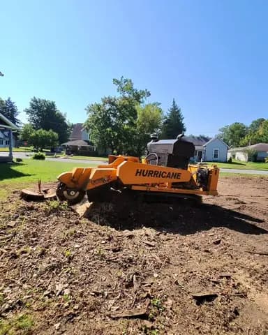 A stump grinder works down a fresh stump on a residential lot.