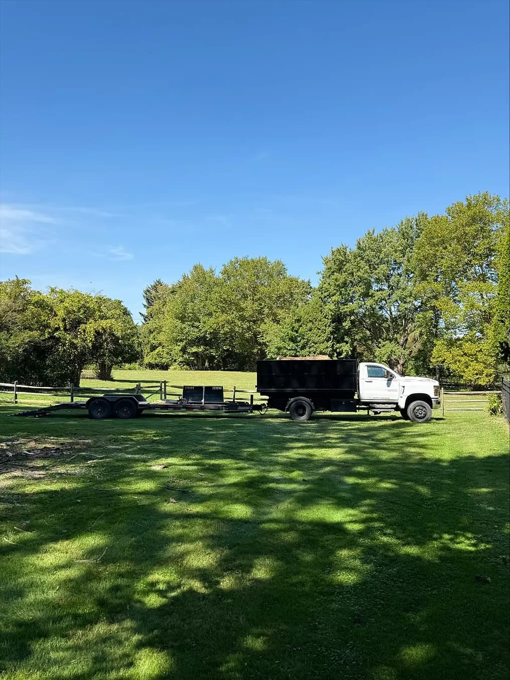 A dump truck and equipment trailer stand on a residential lawn.